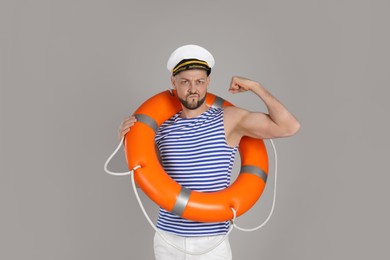 Strong sailor with orange ring buoy showing biceps on grey background