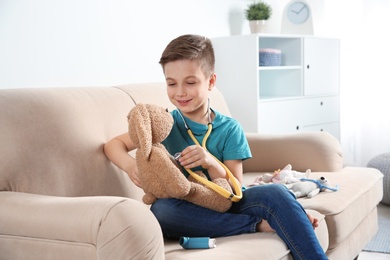 Cute child imagining himself as doctor while playing with stethoscope and toy bunny at home