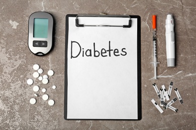 Flat lay composition with word DIABETES, digital glucometer and lancet pen on grey background