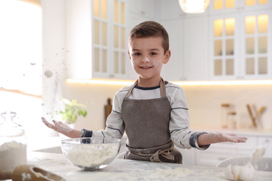 Cute little boy cooking dough at table in kitchen