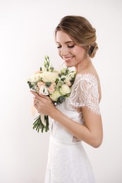 Young bride with elegant hairstyle holding wedding bouquet on white background