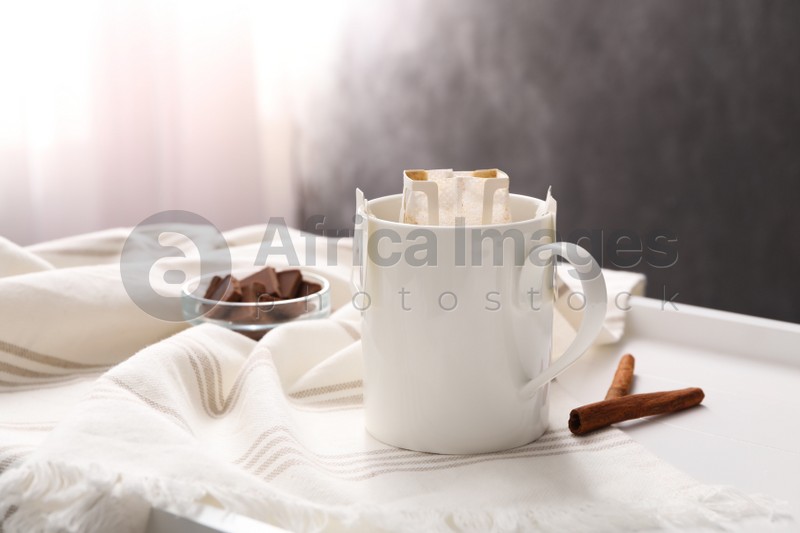 Cup with drip coffee bag and cinnamon on white table, closeup