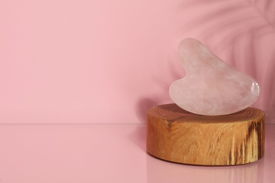 Photo of Rose quartz gua sha tool on pink background, space for text