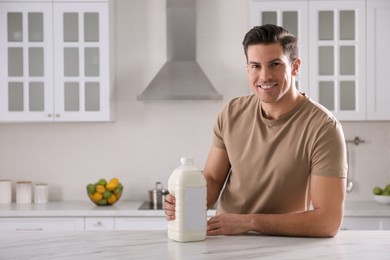 Man with gallon bottle of milk at white marble table in kitchen. Space for text