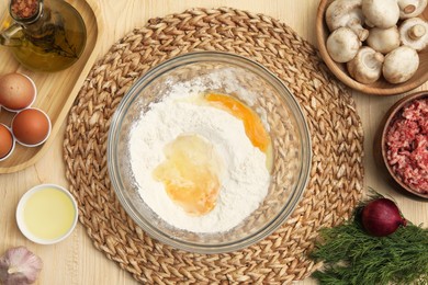 Photo of Bowl with flour, eggs and ingredients on wooden table, flat lay. Process of preparing meat pie