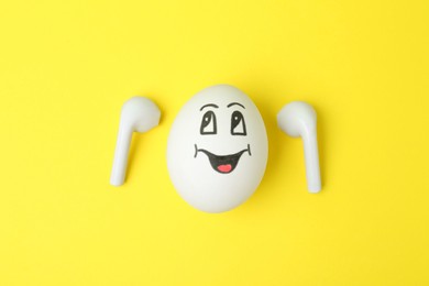 Photo of Egg with drawn happy face and earbuds on yellow background, flat lay