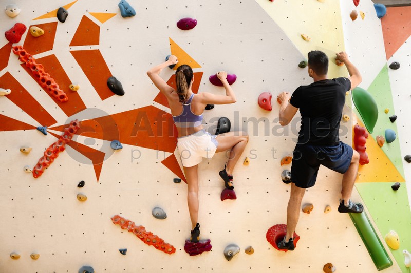 Athletic man and woman climbing wall in gym, back view 
