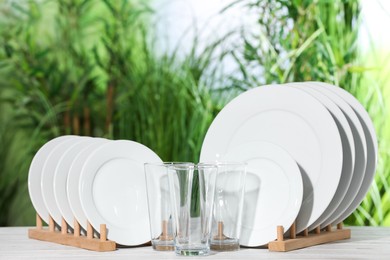 Photo of Set of clean plates and glasses on white table against blurred background