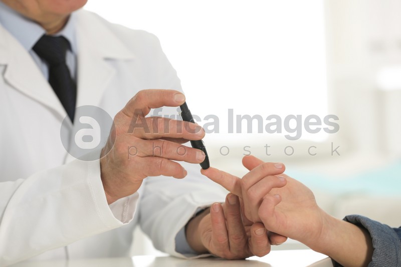 Doctor taking patient's blood sample with lancet pen in hospital, closeup. Diabetes control