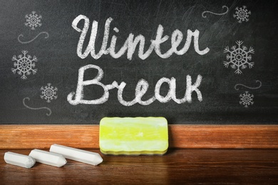 Text Winter break and snowflakes on school blackboard near table with chalk and duster