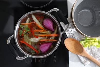 Kitchen counter with bowl, spoon and pot of delicious vegetable bouillon on stove, flat lay