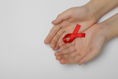 Photo of Little girl holding red ribbon on grey background, top view with space for text. AIDS disease awareness