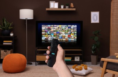 Woman with remote control changing channels while watching TV at home, closeup