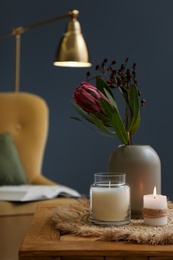 Photo of Vase with beautiful protea flowers and candles on wooden table indoors. Interior elements
