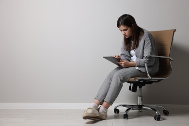 Young woman with bad posture using tablet while sitting on chair near grey wall. Space for text
