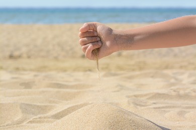 Photo of Child pouring sand from hand on beach, closeup. Fleeting time concept