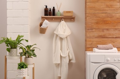 Wooden shelf with toiletries and robe on beige wall in bathroom. Interior design