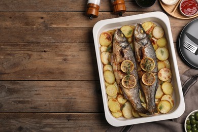 Photo of Baking tray with delicious baked sea bass fish and potatoes on wooden table, flat lay. Space for text