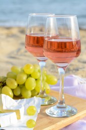 Glasses with rose wine and snacks for beach picnic on sandy seashore, closeup