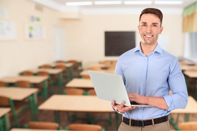 Young teacher with laptop waiting for students in classroom
