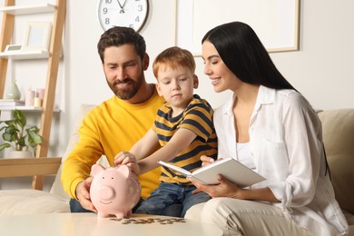 Photo of Happy family with notebook putting coin into piggy bank at home