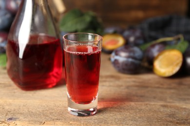 Photo of Delicious plum liquor on wooden table. Homemade strong alcoholic beverage