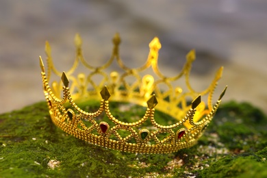 Beautiful golden crown on stone with green moss outdoors, closeup. Fantasy item