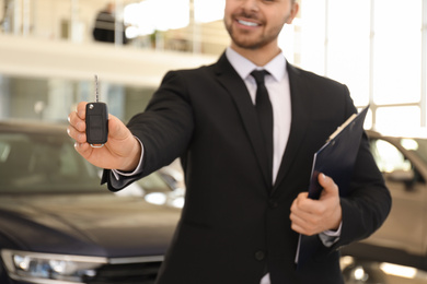 Photo of Salesman with key and clipboard in car salon, closeup