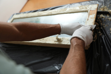 Man repairing old damaged window at table indoors, closeup