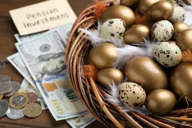 Money, card with phrase Pension Investments near many golden and quail eggs in nest on wooden table