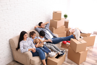 Happy family resting in room with cardboard boxes on moving day