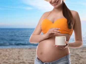 Young pregnant woman with sun protection cream on beach, closeup