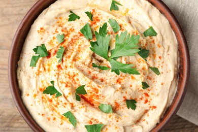 Photo of Top view of tasty hummus with parsley and paprika in bowl on wooden table, closeup