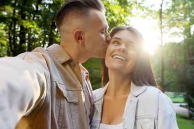 Photo of Affectionate young couple kissing and taking selfie in park