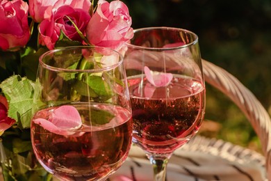 Photo of Glasses of delicious rose wine with petals and flowers outside, closeup