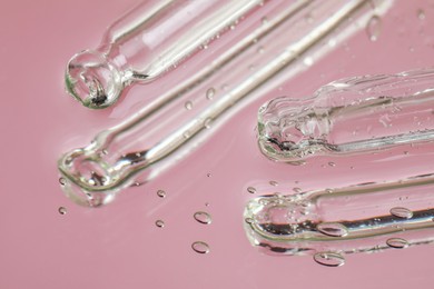 Photo of Pipettes near serum drops on beautiful mirror, closeup. Toned in pink