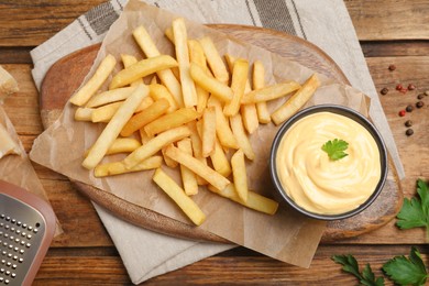 Photo of Delicious French fries and cheese sauce with parsley on wooden table, flat lay