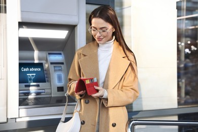 Image of Happy young woman with credit cards near cash machine outdoors