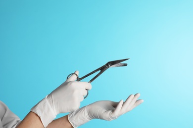 Female doctor holding bandage scissors on color background, closeup view with space for text. Medical object