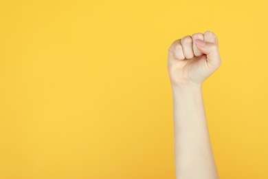Closeup view of woman showing fist as girl power symbol on yellow background, space for text. 8 March concept