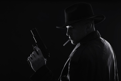 Old fashioned detective with gun smoking cigarette on dark background, black and white effect