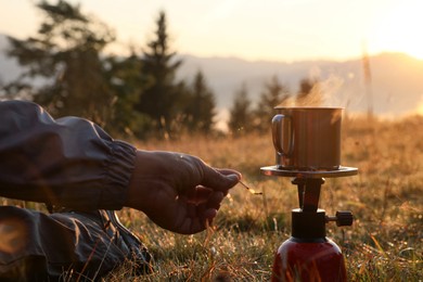 Man making hot drink with portable gas burner in mountain camping, closeup