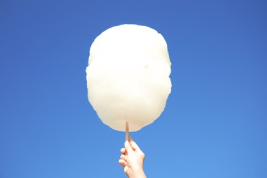 Woman holding white cotton candy against blue sky