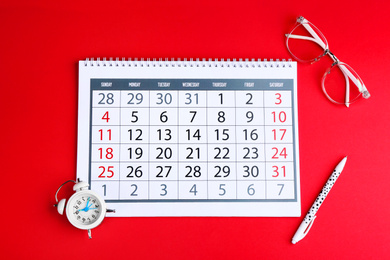 Calendar, glasses and alarm clock on red background, flat lay