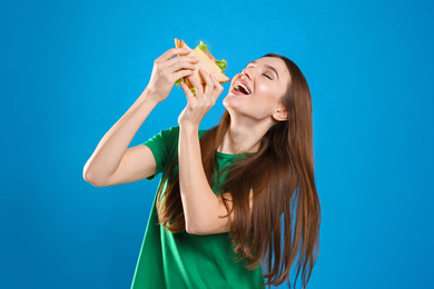 Young woman eating tasty sandwich on light blue background