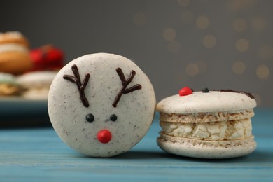 Tasty reindeer Christmas macarons on light blue wooden table against blurred festive lights