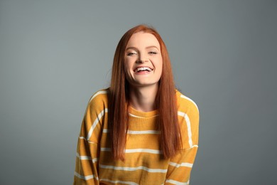 Candid portrait of happy young woman with charming smile and gorgeous red hair on grey background