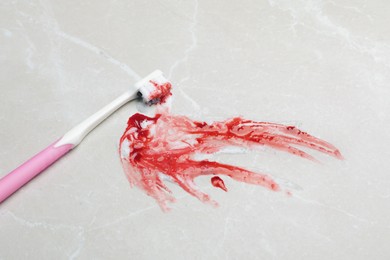 Toothbrush with paste and blood on light grey table. Gum inflammation