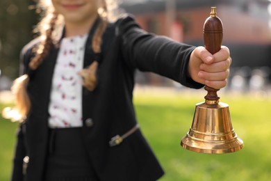 Closeup view of pupil holding school bell outdoors on sunny day