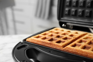 Modern iron with tasty Belgian waffles on table, closeup
